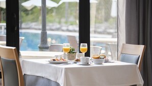 Une table de petit-déjeuner dressée avec des assiettes, des verres et un bol, donnant sur une piscine.
