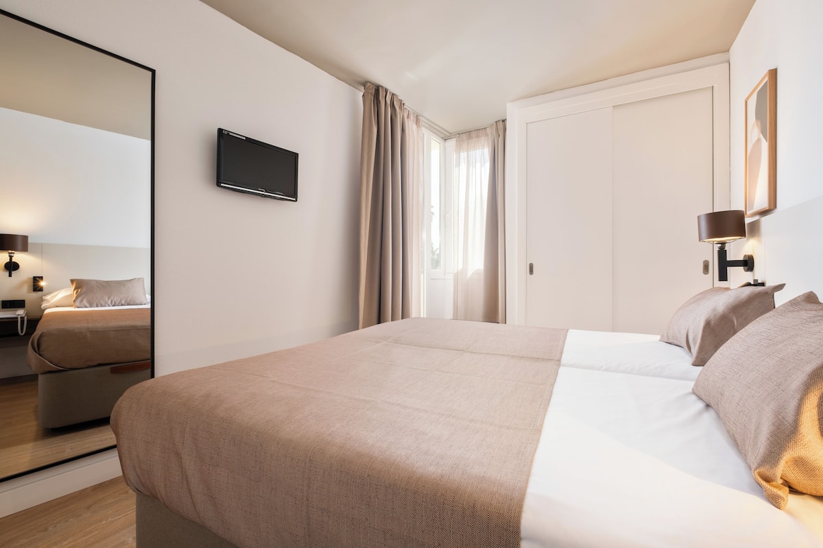A modern hotel room with a large bed, a flat-screen TV, a bedside lamp, and a large mirror.