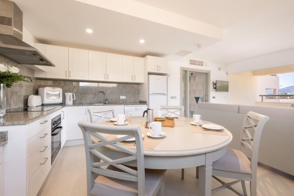 A modern kitchen with white cabinets, a round dining table, and a built-in oven.