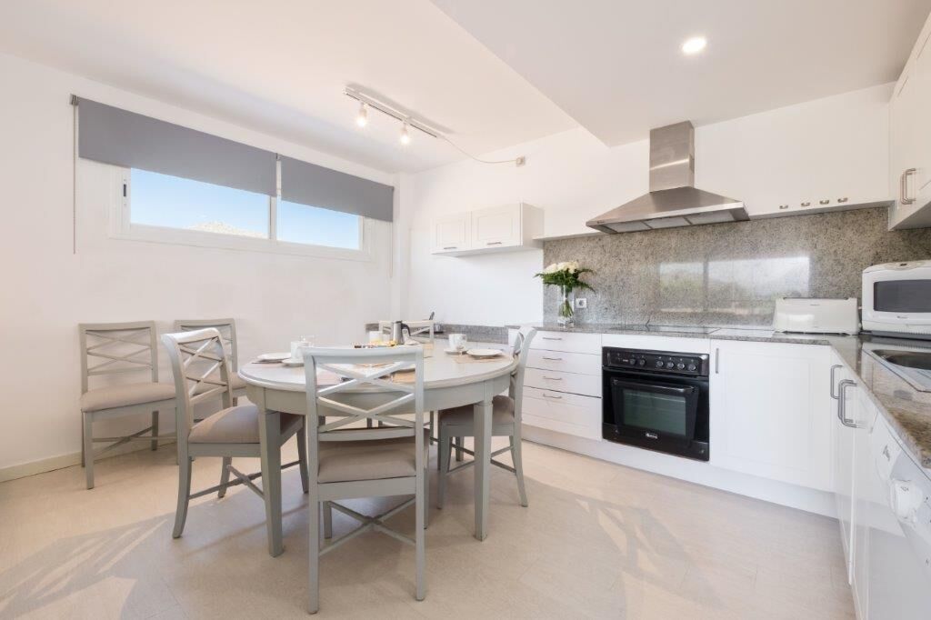 A modern kitchen with white cabinetry, a built-in oven, and a dining area with a round table and chairs.