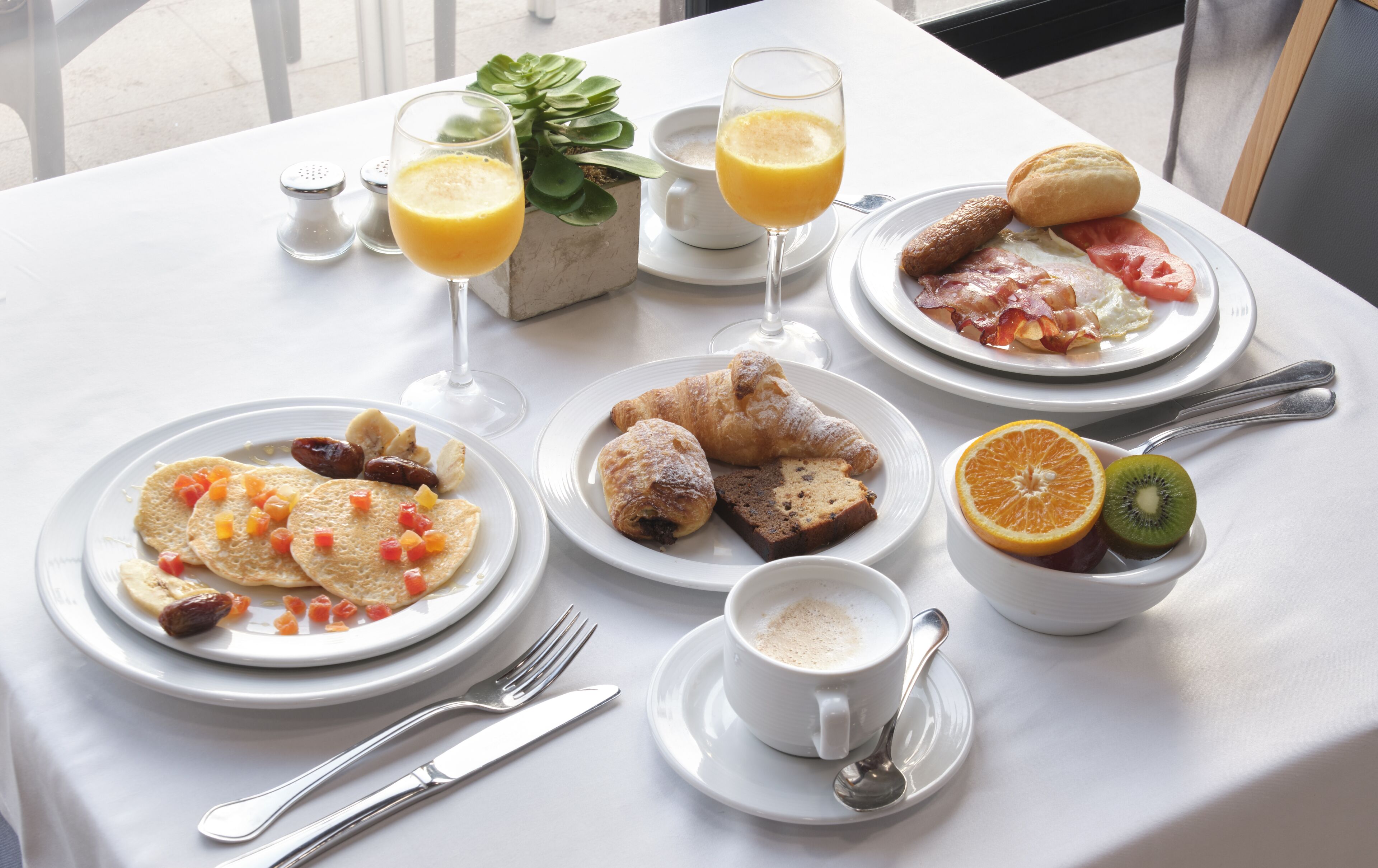 A breakfast table with plates of food, glasses of orange juice, and a cup of coffee.