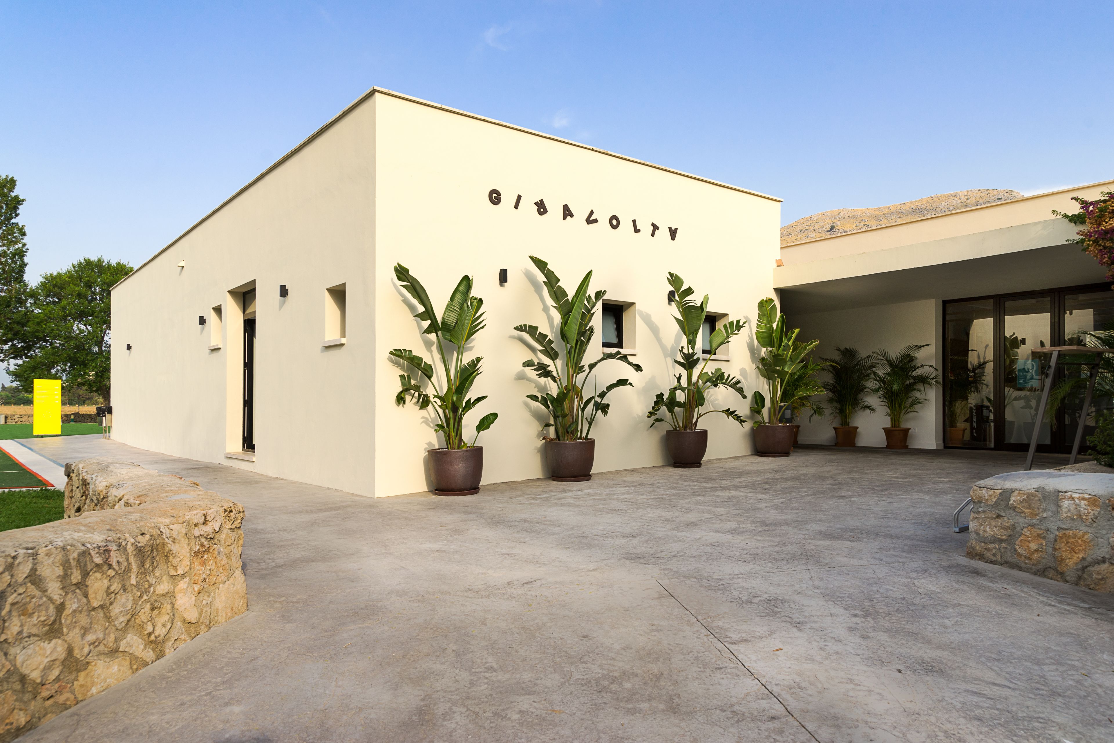 A building with the name "GIBALOTV" on its facade, surrounded by potted plants and a paved area.