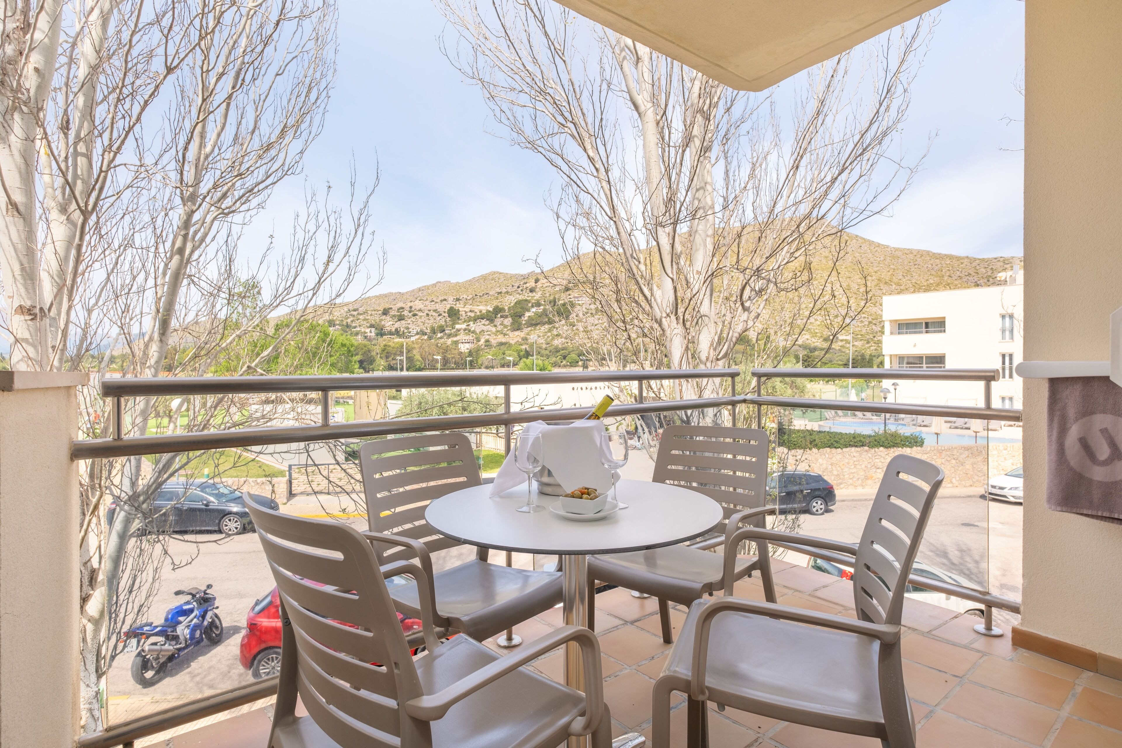 Ein Balkon mit Tisch und Stühlen mit Blick auf parkende Autos und eine hügelige Landschaft.