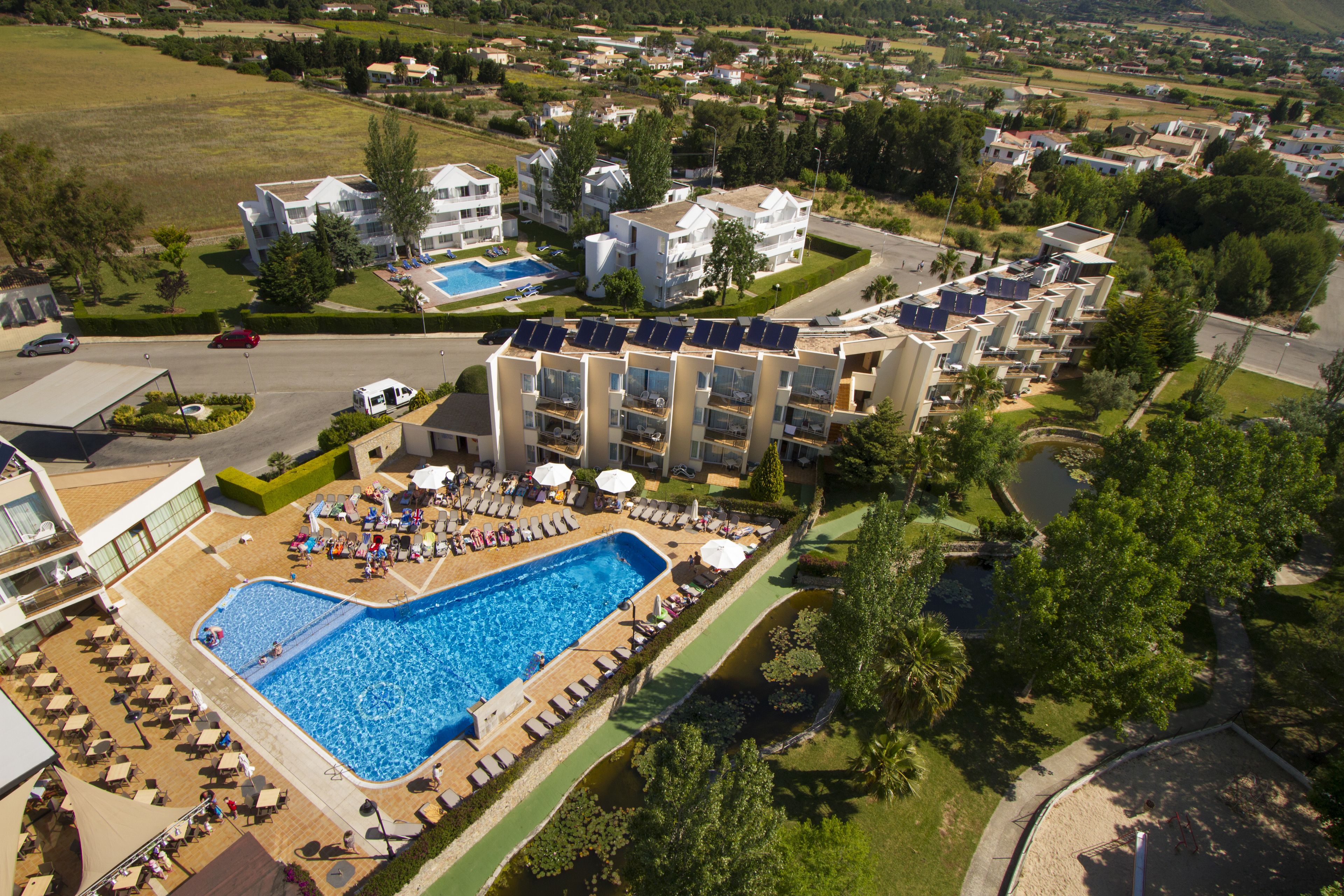 An aerial view of a resort with a swimming pool, sun loungers, and a parking area.