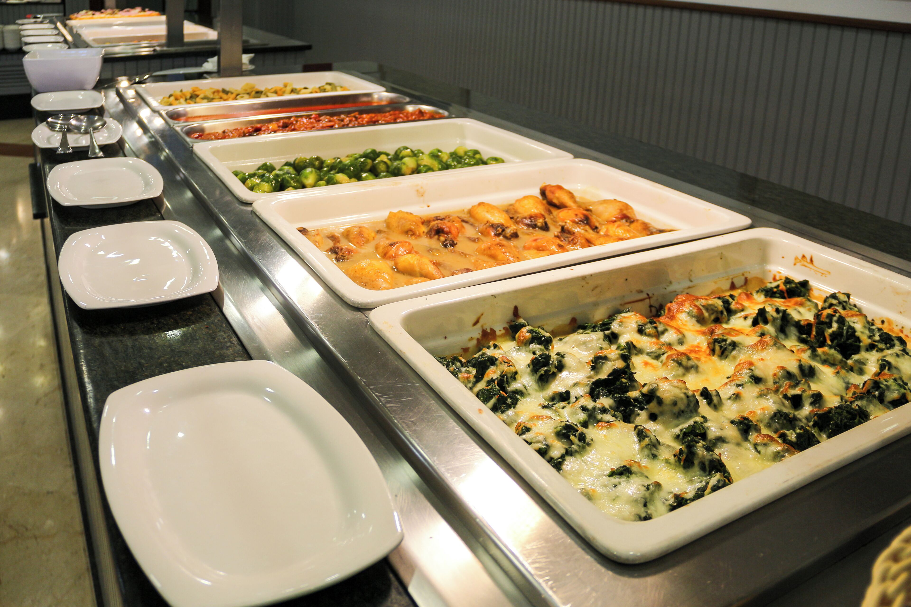 Un buffet proposant divers plats, notamment un gratin d’épinards et de fromage, un plat de pâtes et un plateau de légumes variés.