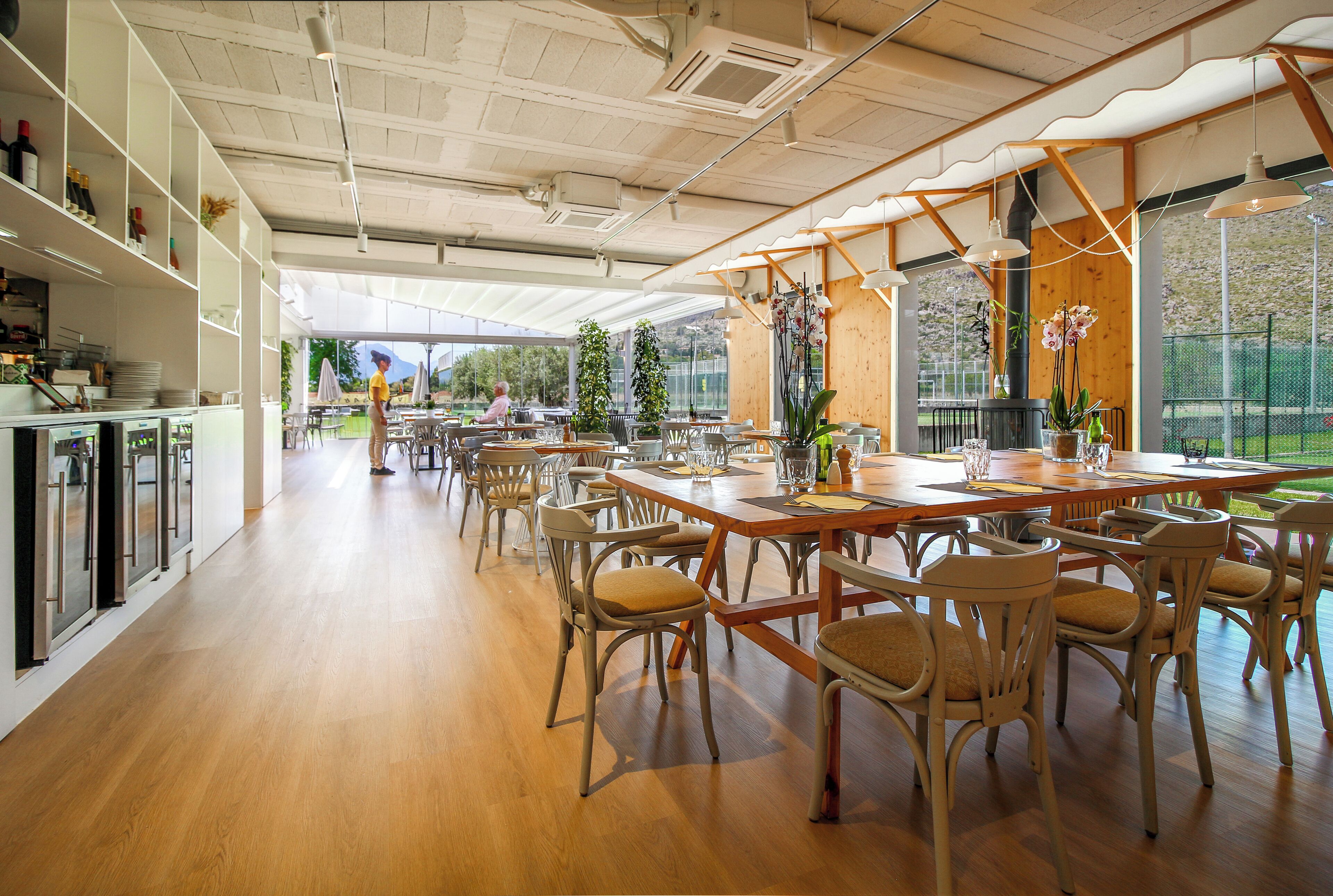 Un comedor amplio con mesas y sillas de madera, una cocina con electrodomésticos de acero inoxidable y grandes ventanales con vistas al exterior.