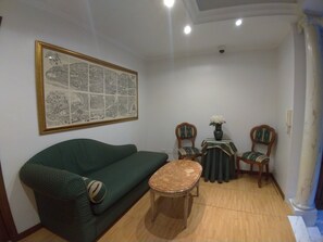 Un salon avec un canapé vert, une petite table ronde, deux chaises et un tableau encadré au mur.
