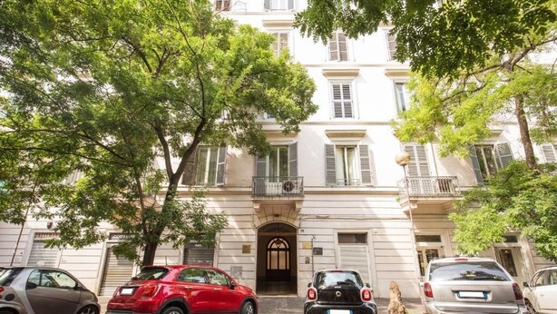 A row of parked cars in front of a building with a classic architectural style, featuring multiple windows and a central entrance. - Residenza dei Quiriti (Rome)