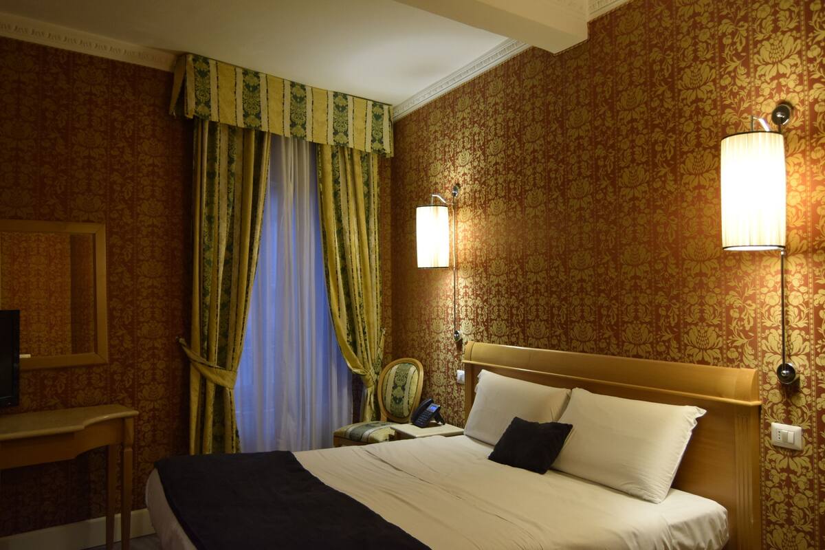A hotel room with a bed, a desk, a telephone, and a lamp.