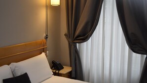 A hotel room with a bed, a bedside phone, a lamp, and curtains. - Residenza dei Quiriti (Rome)