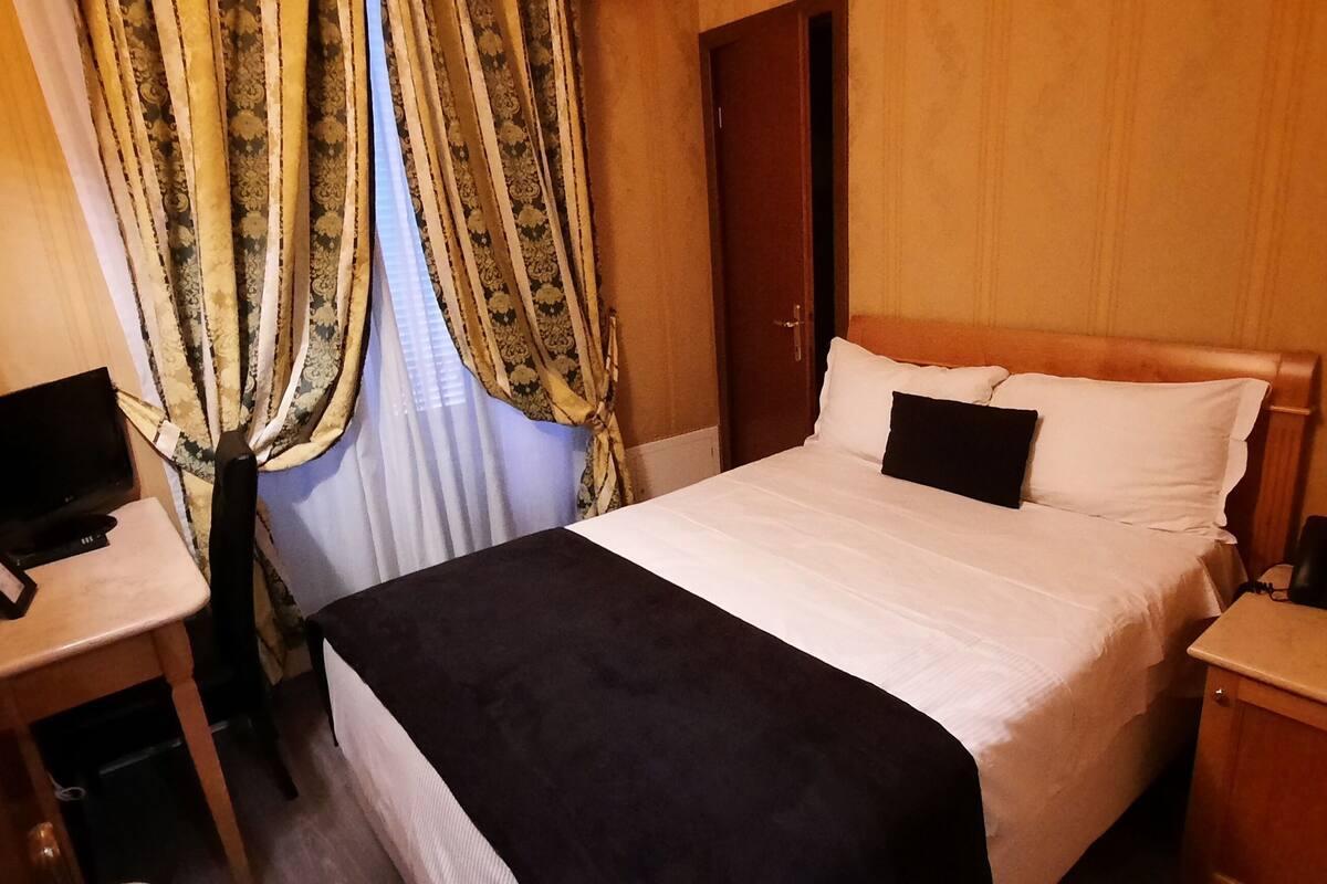 A hotel room with a bed, a desk with a computer, a telephone, and a lamp.