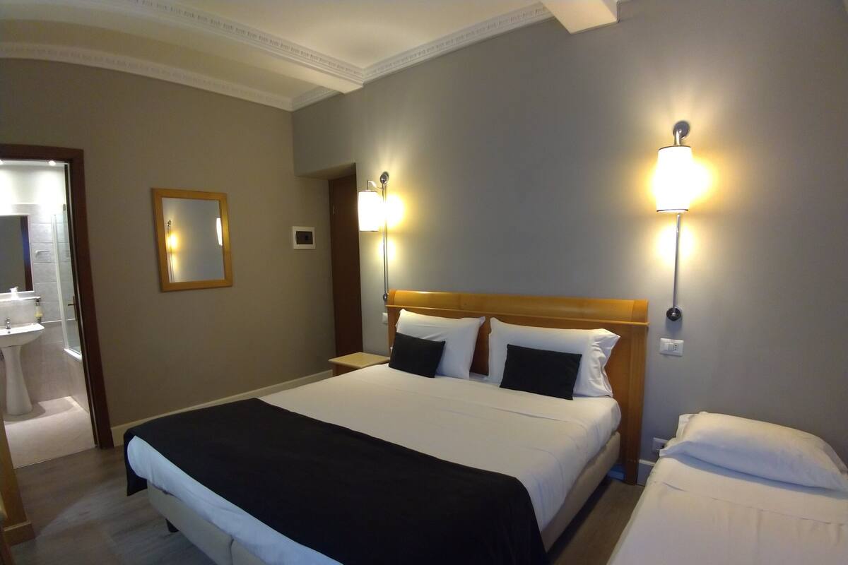 A hotel room with a large bed, bedside lamps, a mirror, and a bathroom visible through an open door.