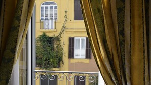 A balcony with wrought iron railings and a view of a yellow building with shutters. - Residenza dei Quiriti (Rome)