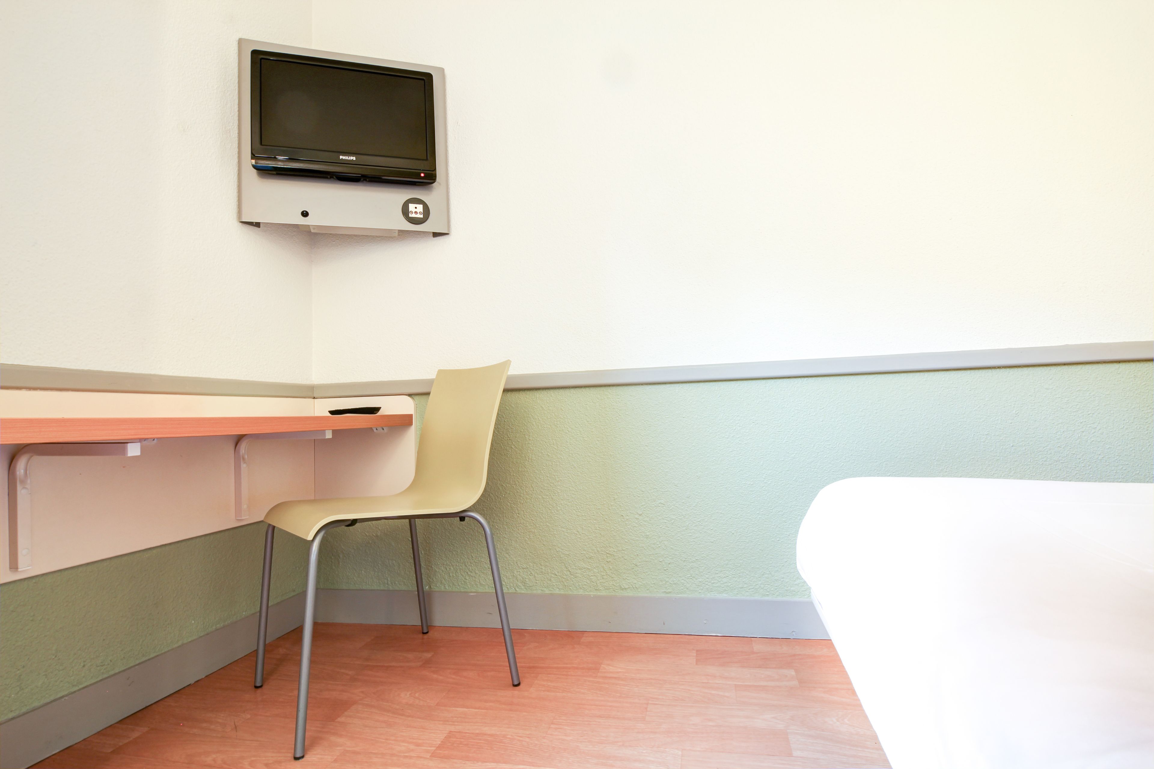 A room with a single chair, a small table, and a mounted television.