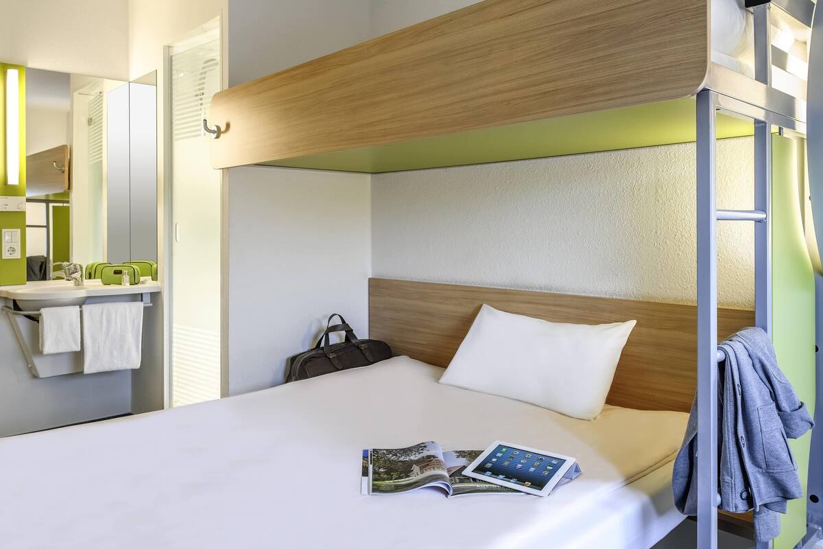 A bunk bed with a wooden headboard, a bedside table with a magazine, and a suitcase.