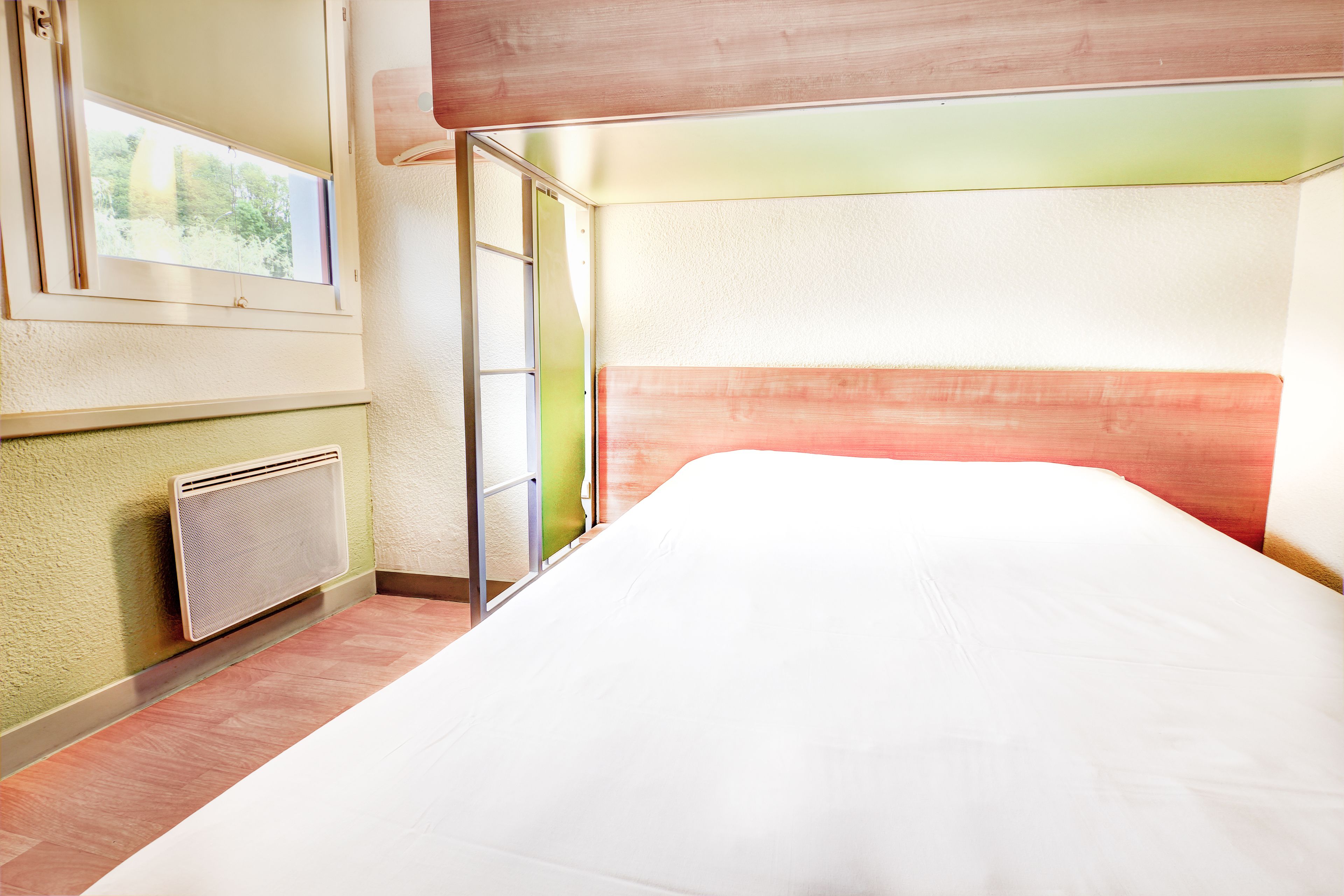 A hotel room with a bed, a window, a radiator, and a door.