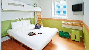 Une chambre d’hôtel avec un lit superposé, une table de chevet avec une télévision, une fenêtre donnant sur un paysage agréable et un sac vert posé sur le sol.