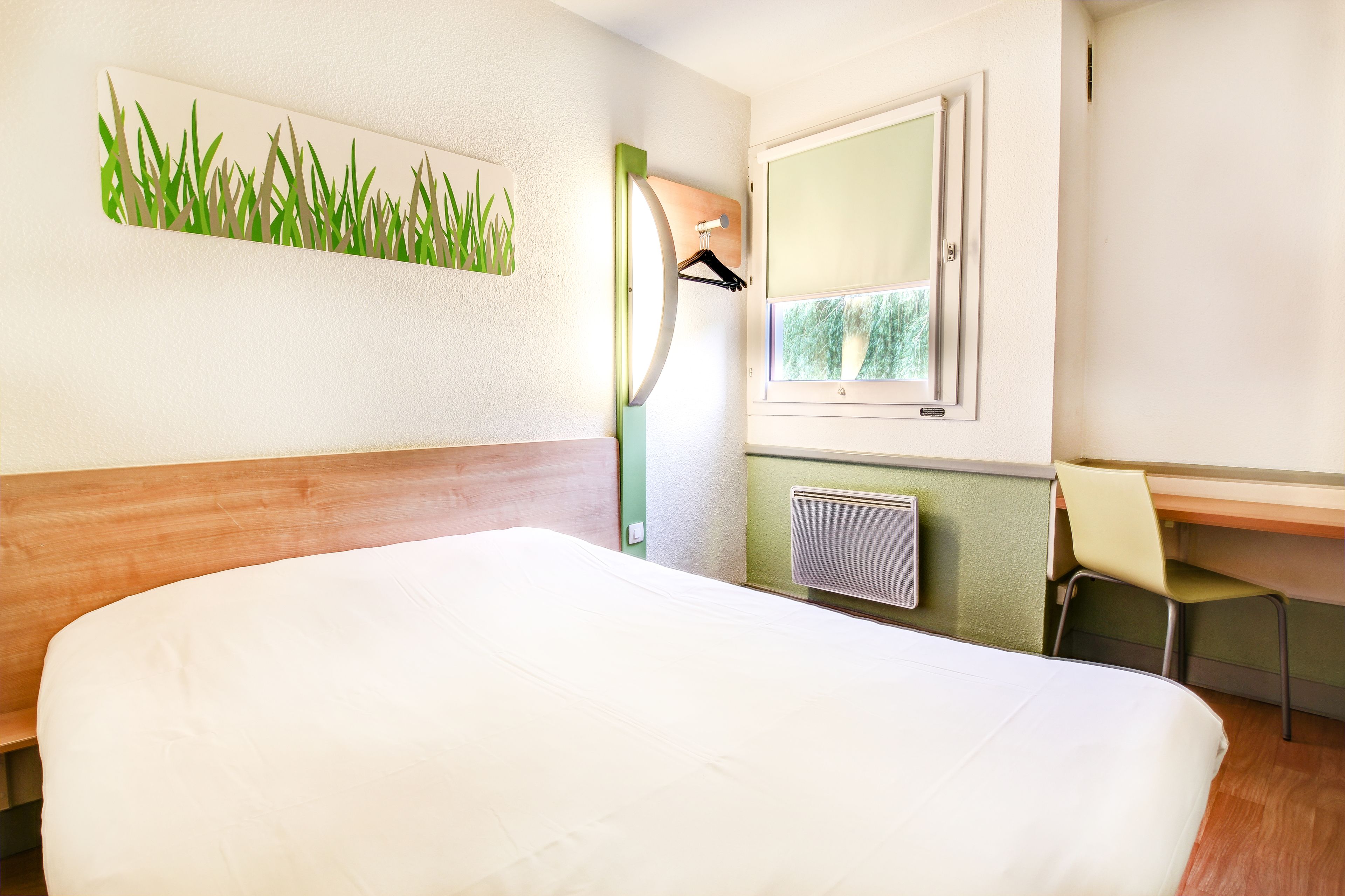 Une chambre d’hôtel équipée d’un lit, d’un bureau, d’une chaise, d’un miroir et d’un radiateur fixé au mur.