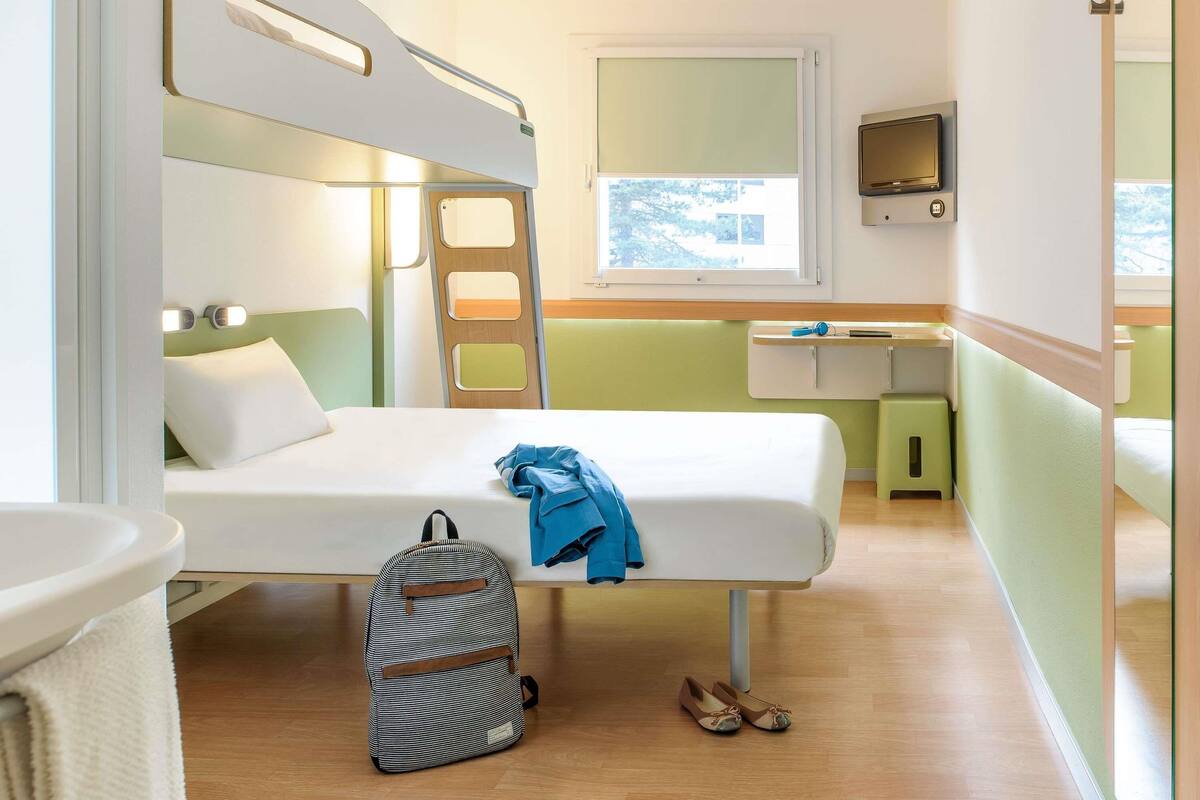 A compact room with bunk beds, a small desk, a TV, and a window with a view.