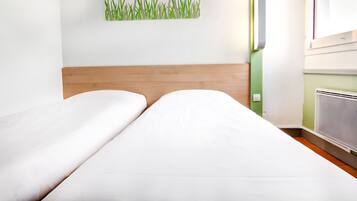 Ein Hotelzimmer mit zwei Betten, einem Holz-Kopfteil, einem an der Wand befestigten Kunstwerk mit Grasdarstellung und einem Heizkörper.