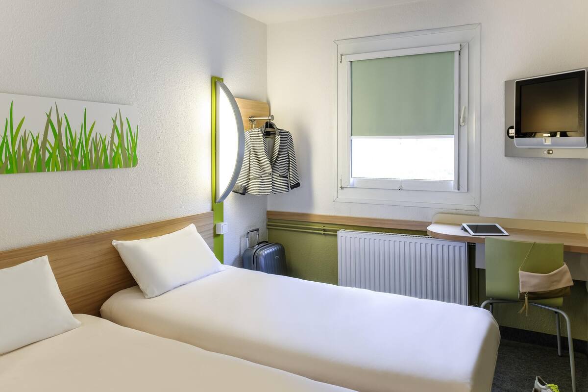 A hotel room with two beds, a desk with a computer, a TV, and a window with a view.