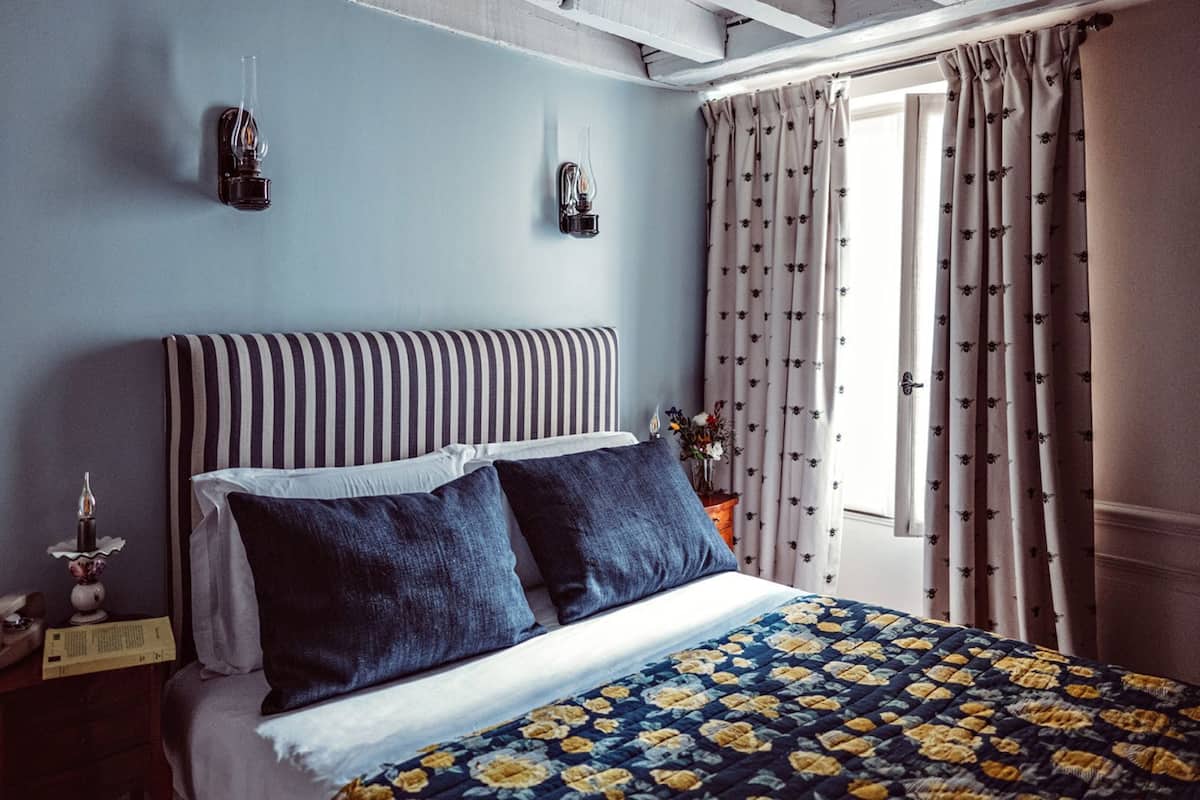 Un lit avec une tête de lit à rayures, une couvre-lit à motifs floraux et une table de chevet avec une lampe et un téléphone.