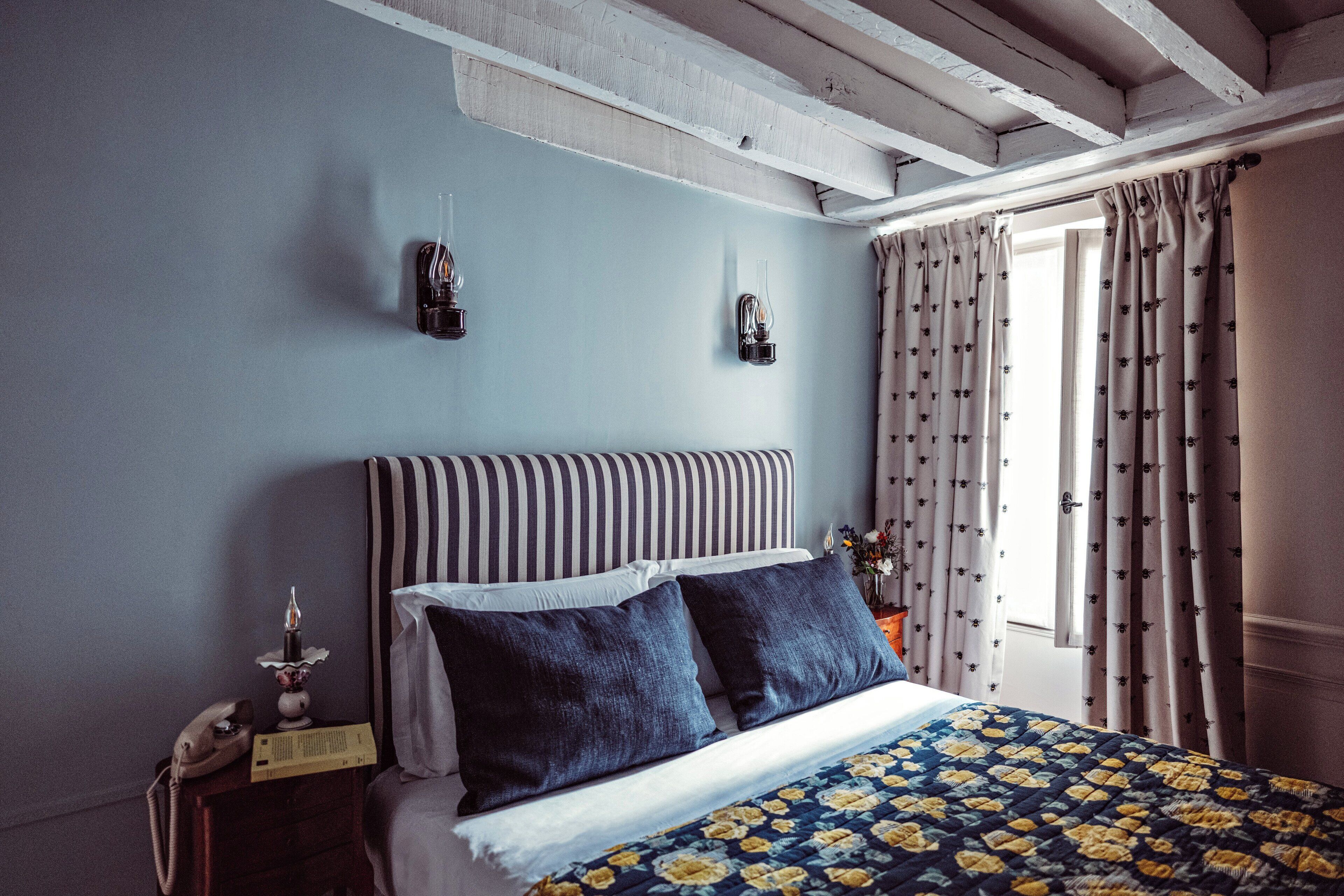 Una camera da letto con una testiera a righe, un letto con una coperta a fiori, un telefono sul comodino e tende decorate con un motivo.