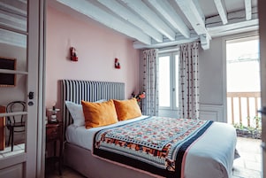 Un dormitorio con cama, mesita de noche, una silla y ventana con cortinas.