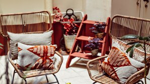 Des chaises en osier avec des coussins, une chaise rouge et une petite table agrémentée d’objets décoratifs.