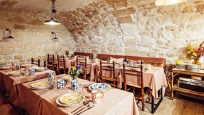Un coin repas rustique avec des murs en pierre, des tables en bois et des nappes à carreaux.