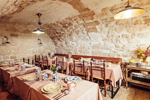 A rustic dining area with stone walls, wooden tables, and checkered tablecloths.