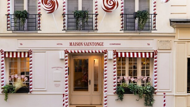 La façade d’un hôtel, avec une enseigne indiquant « HÔTEL MAISON SAINTONGE », et des balcons ornés de stores rayés et de plantes.