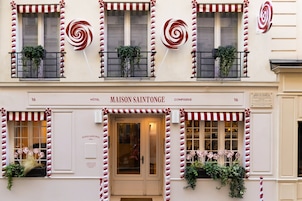 A hotel facade with a sign reading "MAISON SAINTONGE HOTEL" and balconies with striped awnings and plants.