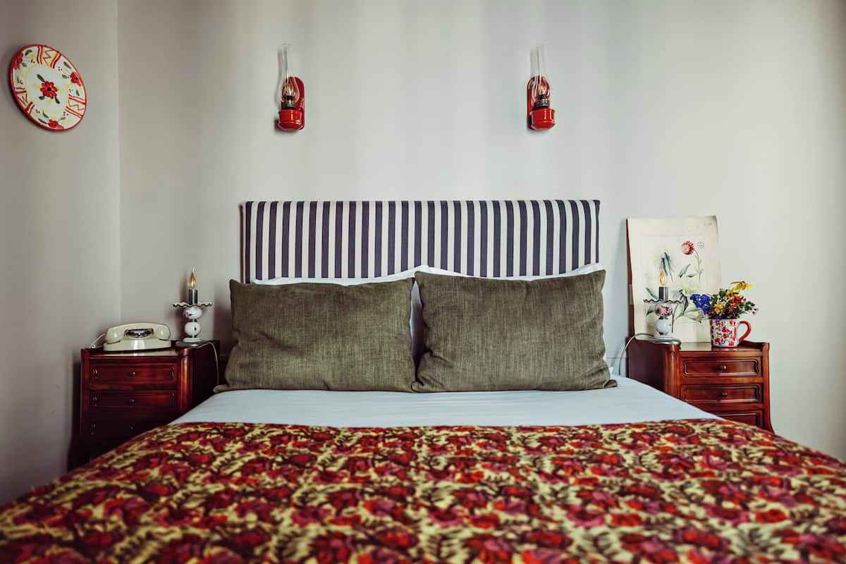 Un lit bien fait, avec une tête de lit à rayures, une couvre-lit à motifs floraux et un téléphone ancien posé sur une table de chevet en bois.