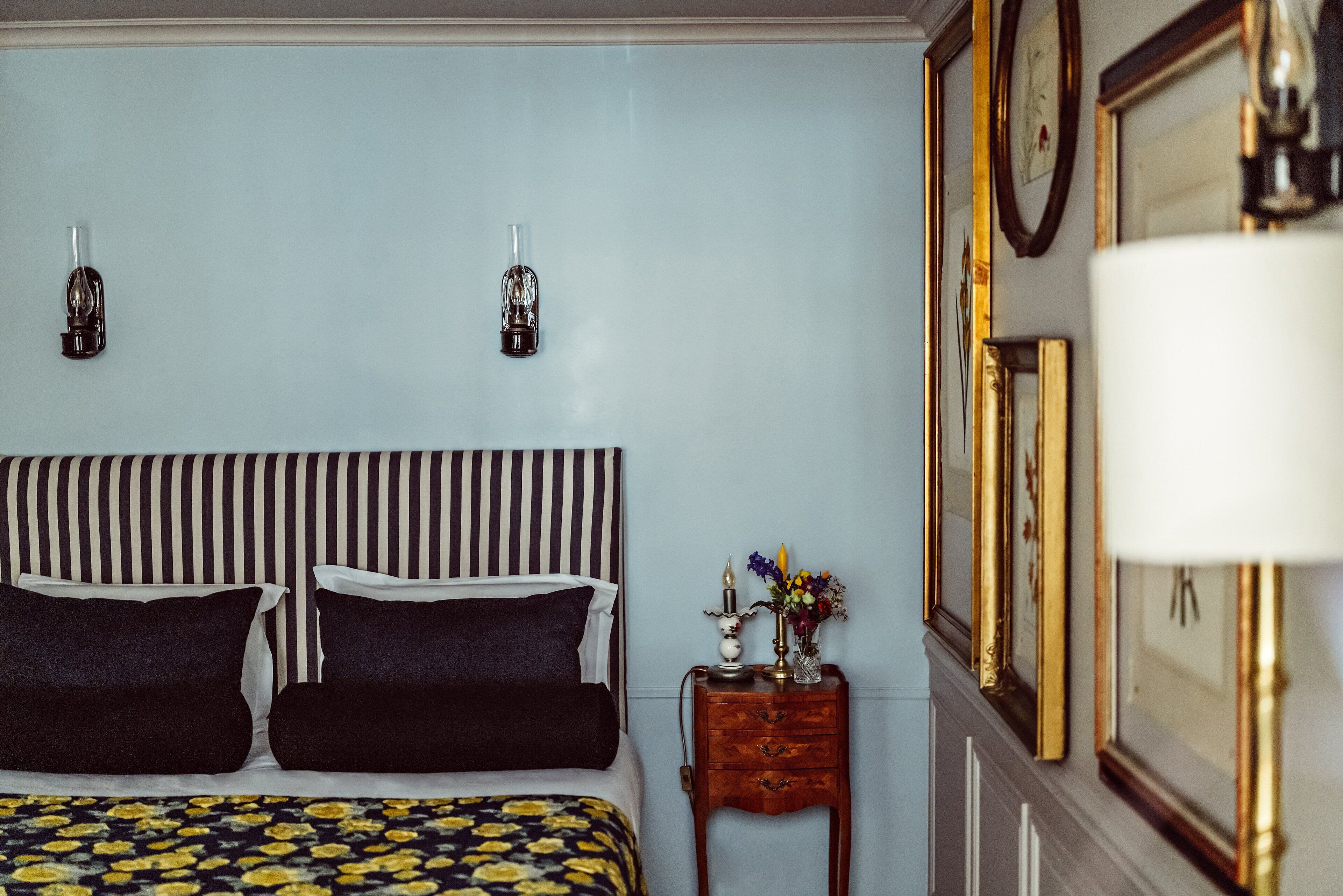 A bedroom with a striped headboard, a bedside table with a lamp, and framed pictures on the wall.