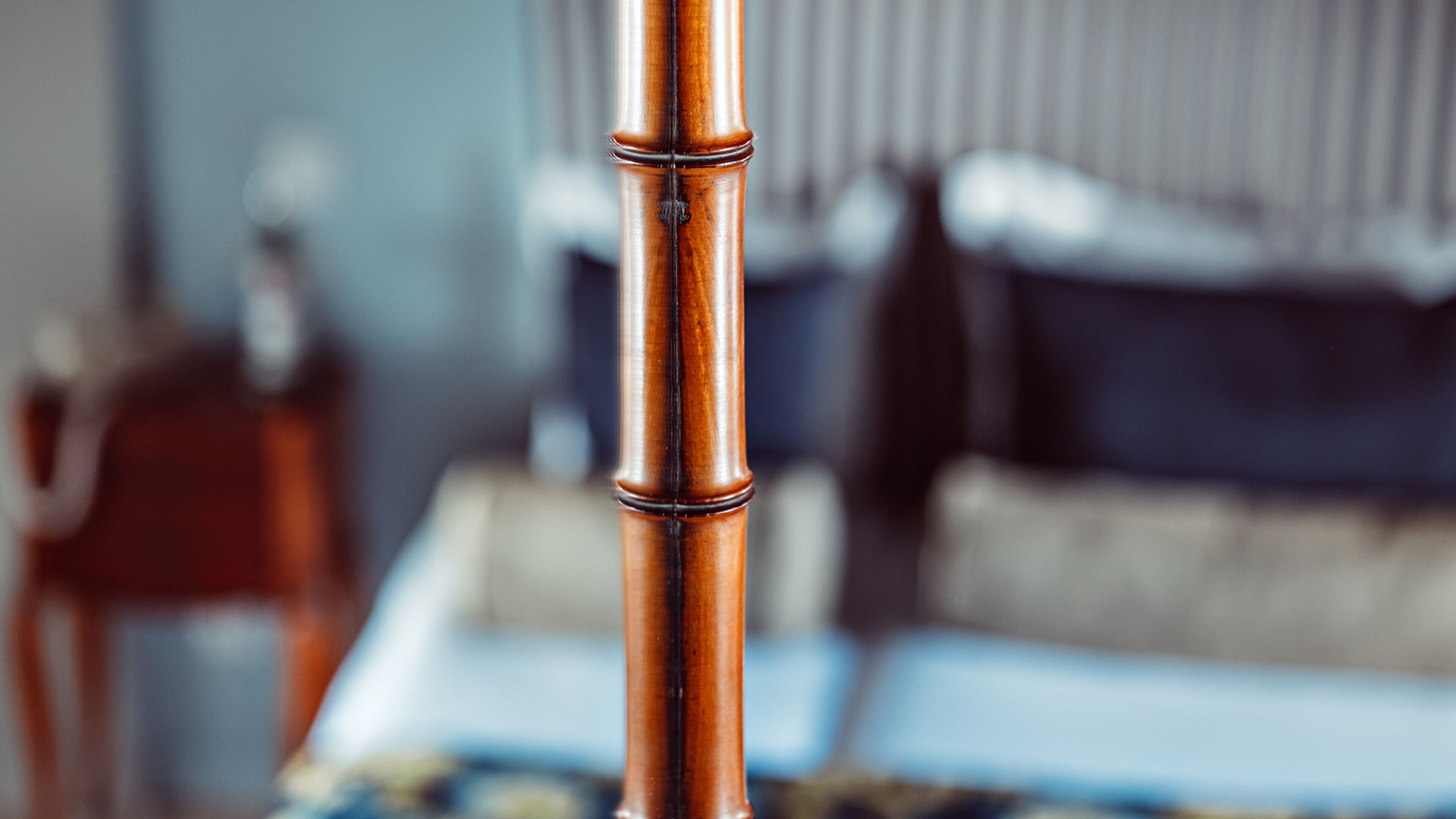 A close-up of a bamboo-style bed frame with a blurred background of a room.