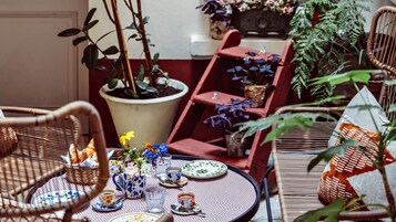 A cozy outdoor seating area with wicker chairs, a round table set with plates, cups, and a vase of flowers.