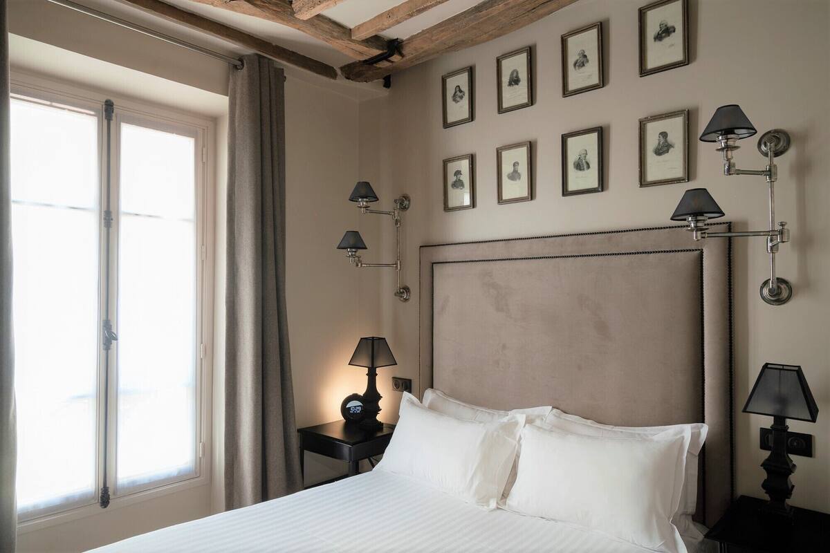A hotel room with a large bed, a headboard with a tufted design, multiple wall-mounted lamps, and framed portraits on the wall.
