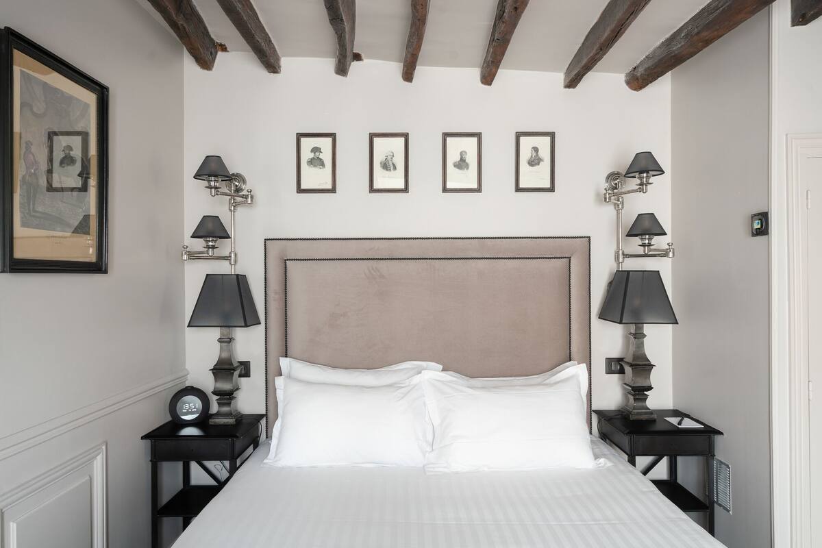 A hotel room with a large bed, two bedside tables with lamps, a clock, and framed portraits on the wall.