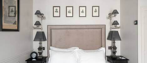 Habitación de hotel con una cama grande, dos mesitas de noche con lámparas, un reloj y retratos enmarcados en la pared.