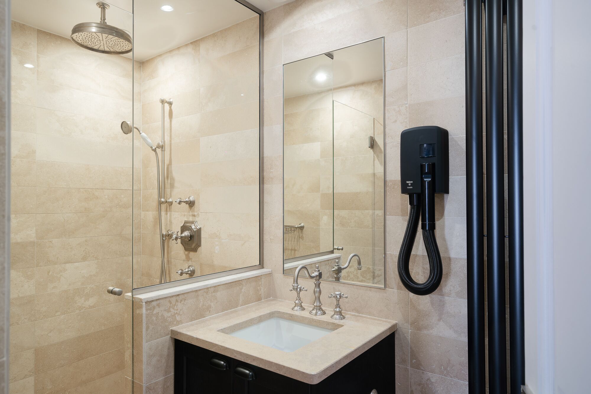 Ein modernes Badezimmer mit Duschabtrennung aus Glas, einem Waschtisch mit Becken und einer Handbrause.