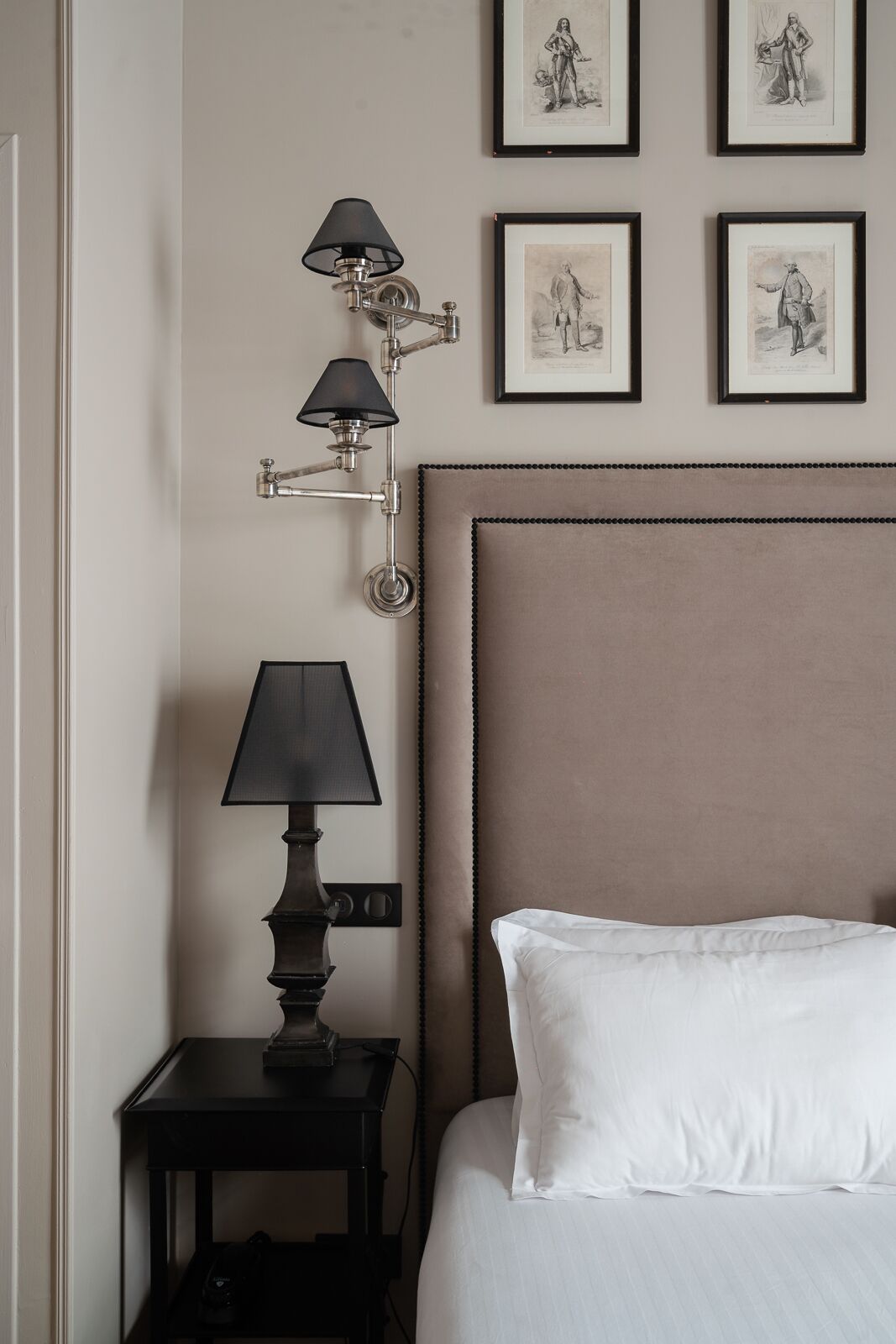 A hotel room with a bed, a nightstand with a lamp, and three framed pictures on the wall.
