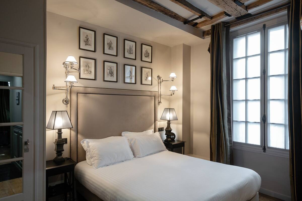 A neatly made bed with white linens, a wooden headboard, and bedside lamps. There are framed pictures on the wall above the bed.
