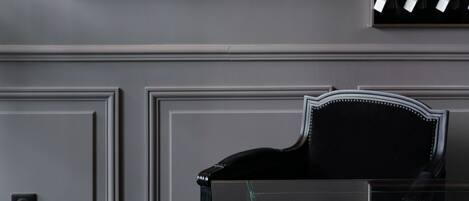 A framed historical painting, a display of wine bottles, and a piano in a room with a glass table.
