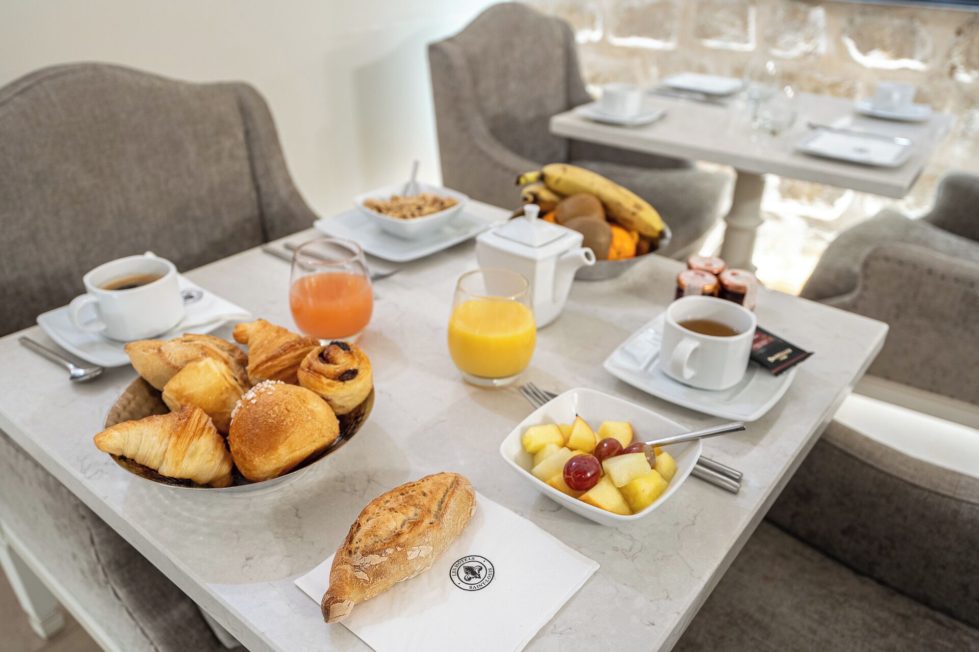 Una mesa de desayuno con cruasanes, fruta, café y jugo.