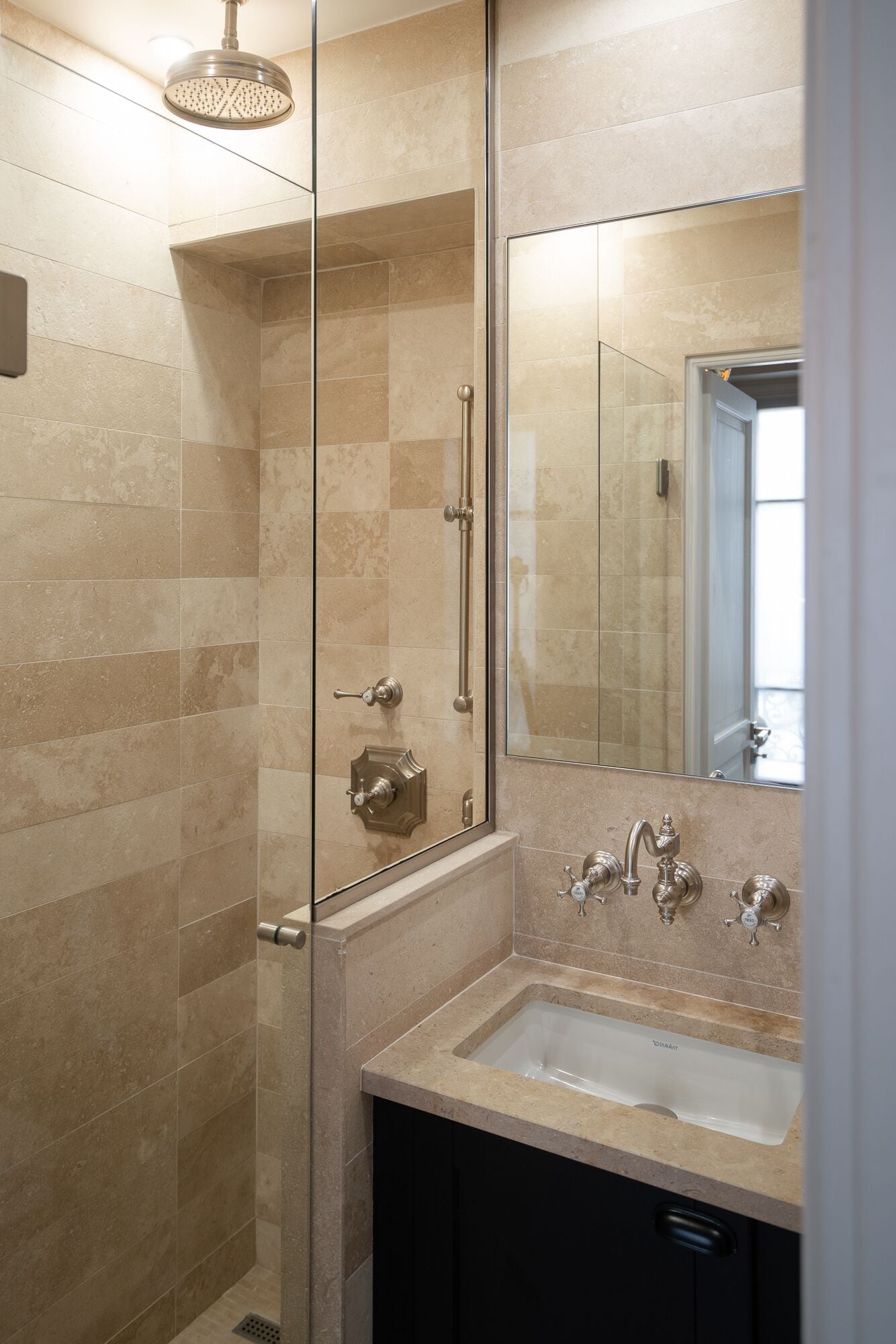A modern bathroom with a glass-enclosed shower, a sink with two faucets, and a large mirror.