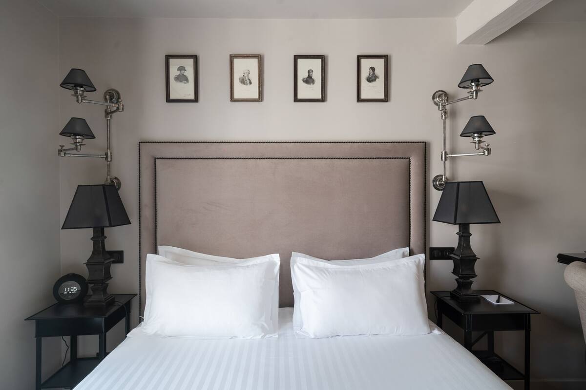 A hotel room with a large bed, two bedside tables, and four wall-mounted lamps.