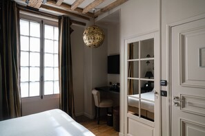 A bedroom with a bed, a desk, a chair, a hanging light fixture, and a wardrobe.