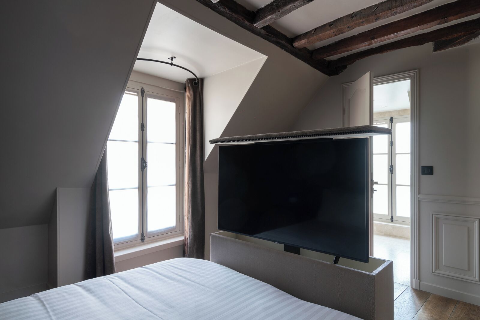 A bedroom with a large bed, a built-in TV, and a sloped ceiling with exposed beams.