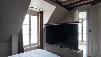 A bedroom with a large bed, a built-in TV, and a sloped ceiling with exposed beams.